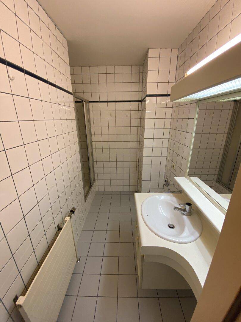 Badezimmer mit weißen Fliesen, Waschbecken und Duschbereich mit Glasabtrennung.