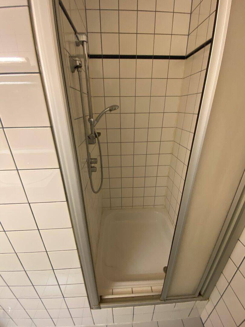 Duschbereich mit weißen Fliesen und einfacher Duscharmatur in einem Badezimmer.