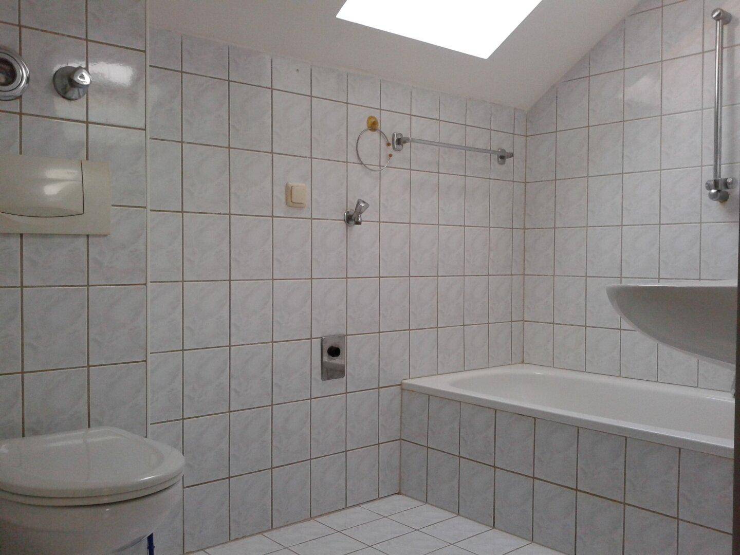 Gefliestes Badezimmer mit Badewanne, Toilette, Waschbecken und Dachfenster für Tageslicht.