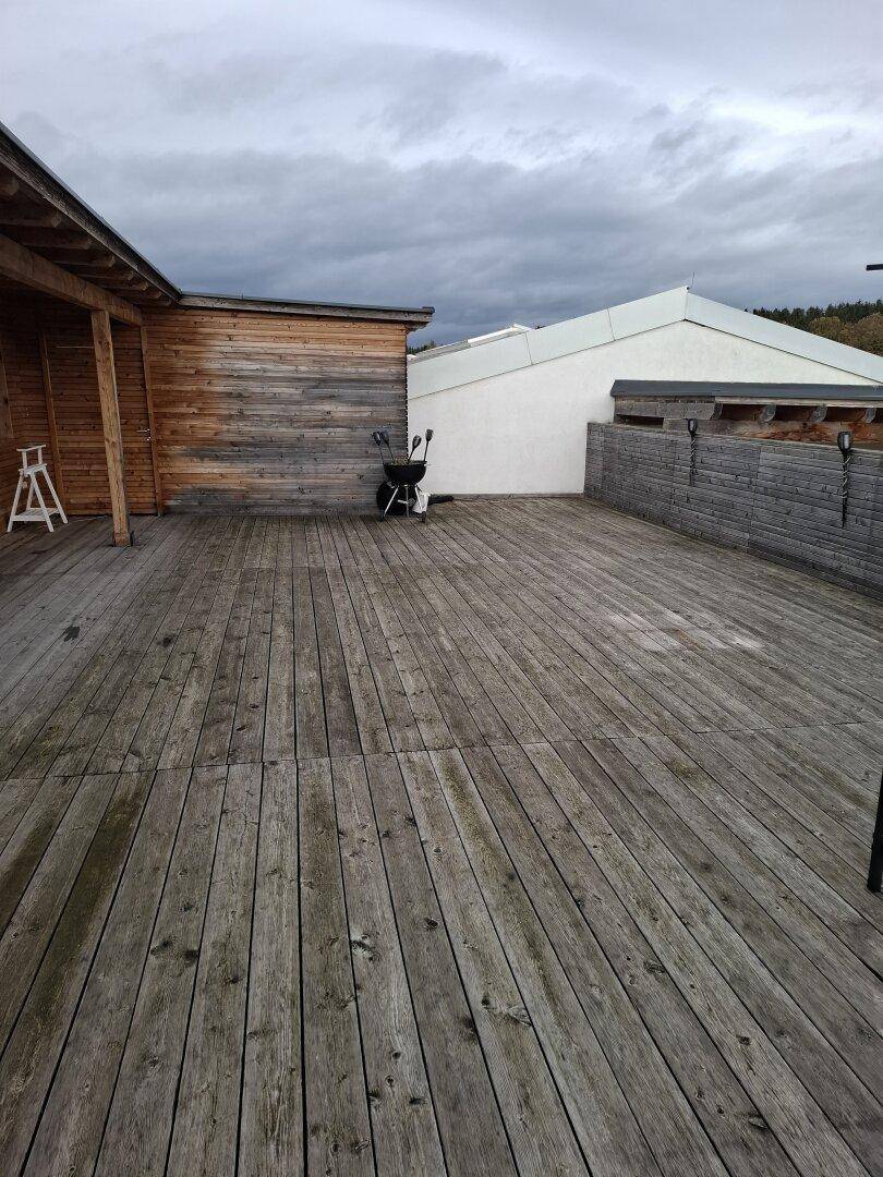 Große Holzterrasse mit Grill und Holzwänden unter bewölktem Himmel.