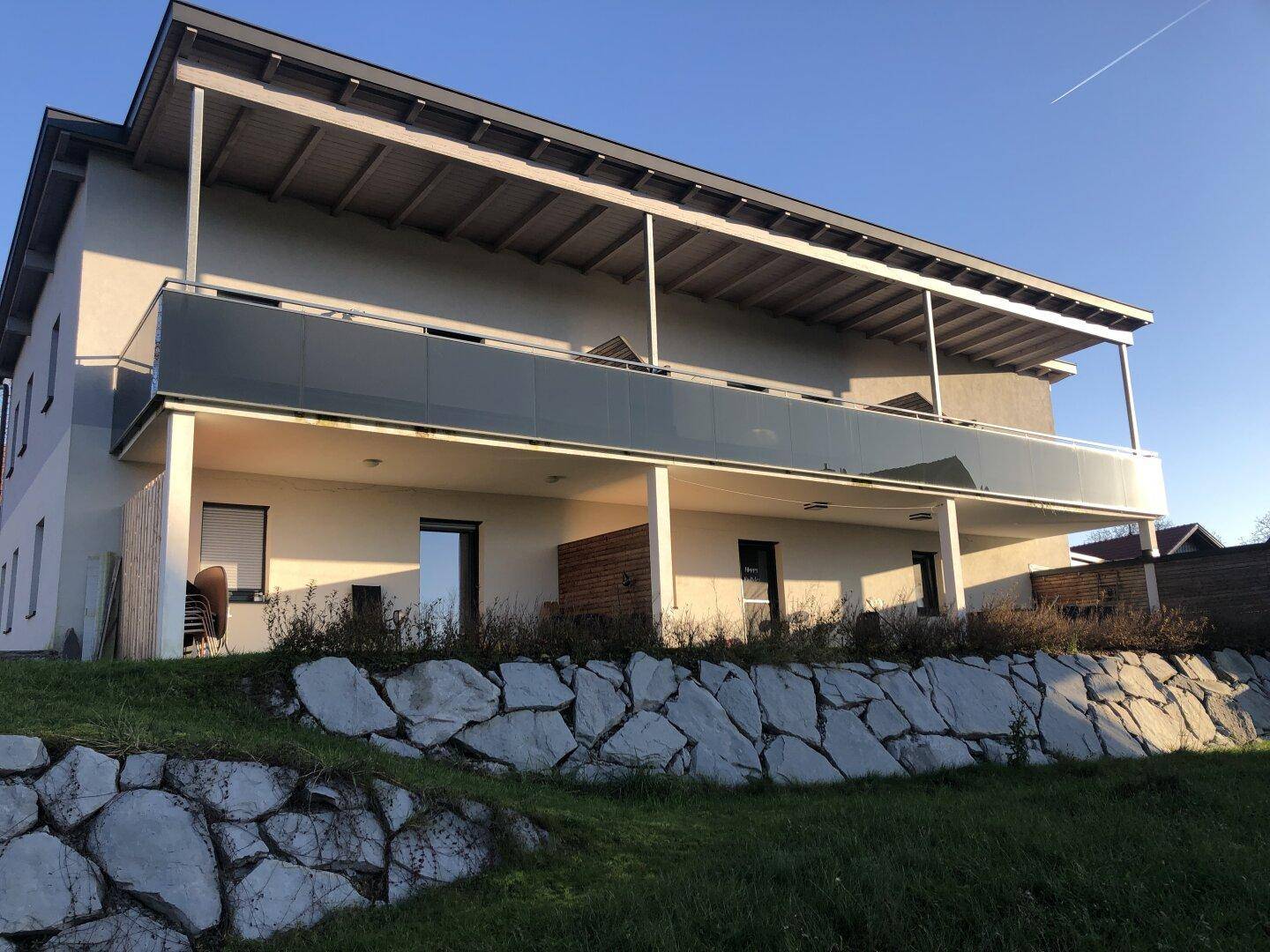 Modernes Wohngebäude mit überdachten Balkonen und Terrassen, umgeben von einer Natursteinmauer.