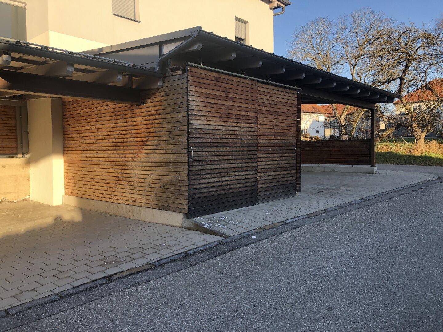 Carports mit Holzverkleidung und gepflasterter Fläche, angrenzend an das Wohngebäude.