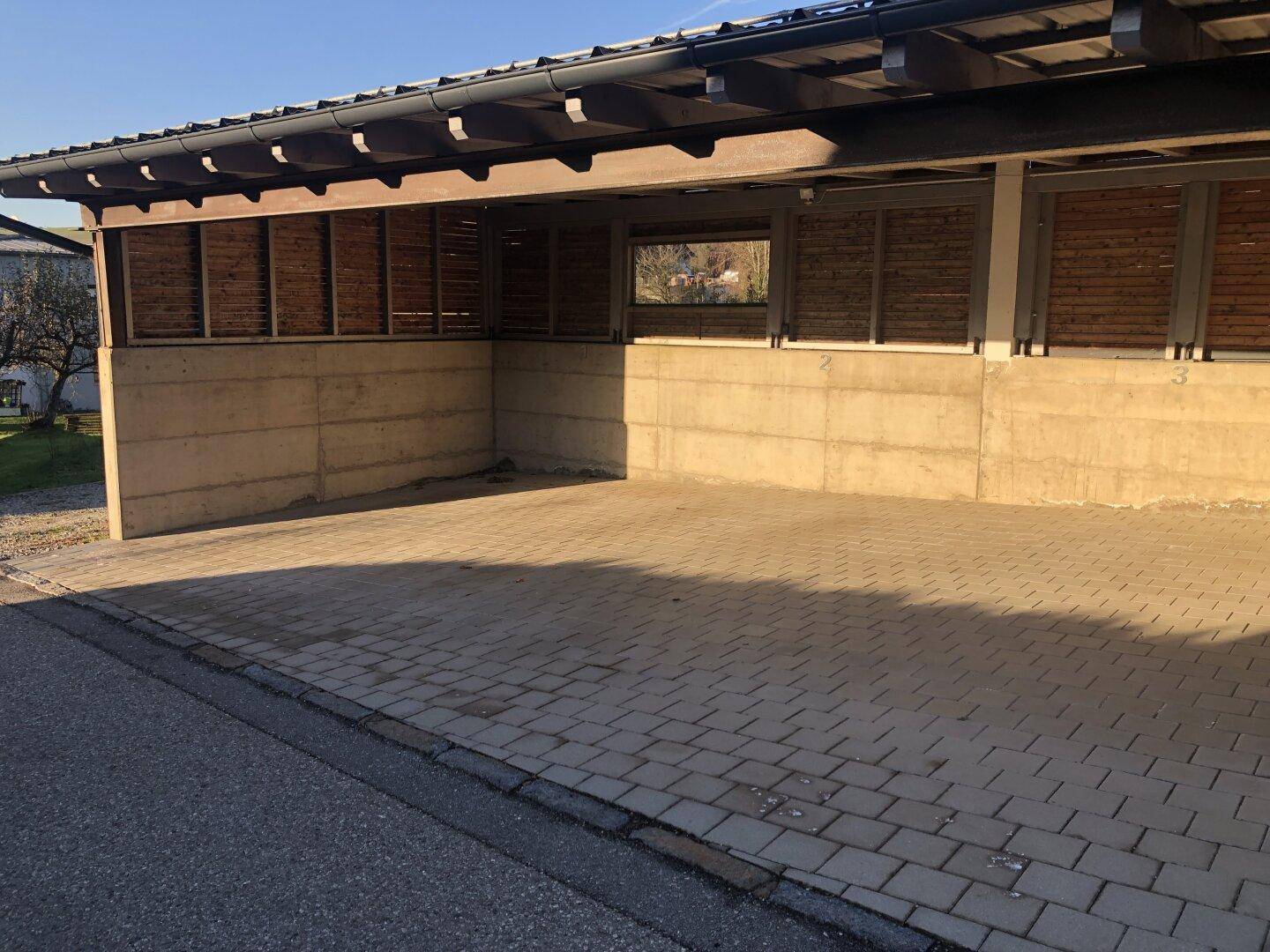Überdachte Carports mit gepflastertem Boden und Holzlamellen als Seitenwände.
