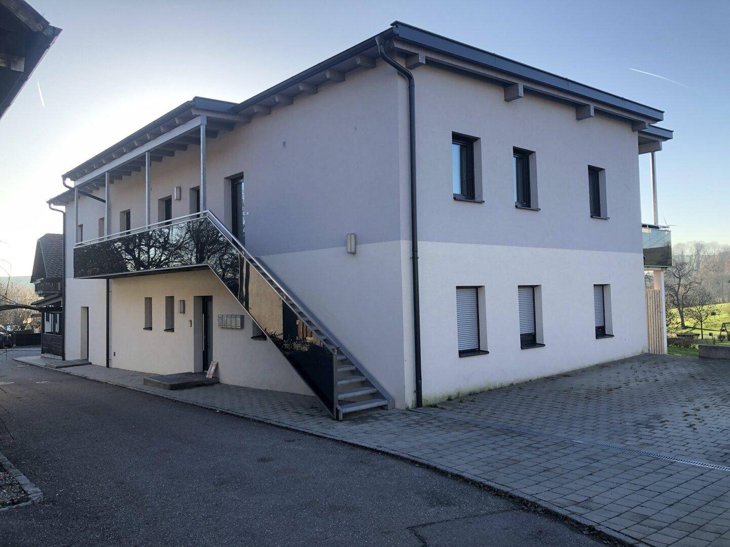 Moderne Gebäudefassade mit Außentreppe und Balkonen, in heller Farbgebung.