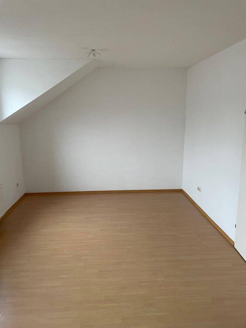 Leerer Raum mit Dachschräge, hellem Laminatboden und weißen Wänden, bereit zur individuellen Gestaltung.