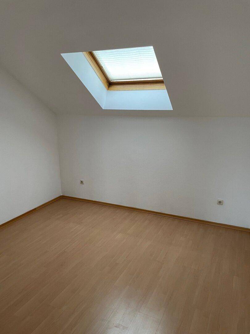 Heller Raum mit Dachfenster, Laminatboden und weißen Wänden, ideal für Schlaf- oder Arbeitszimmer.