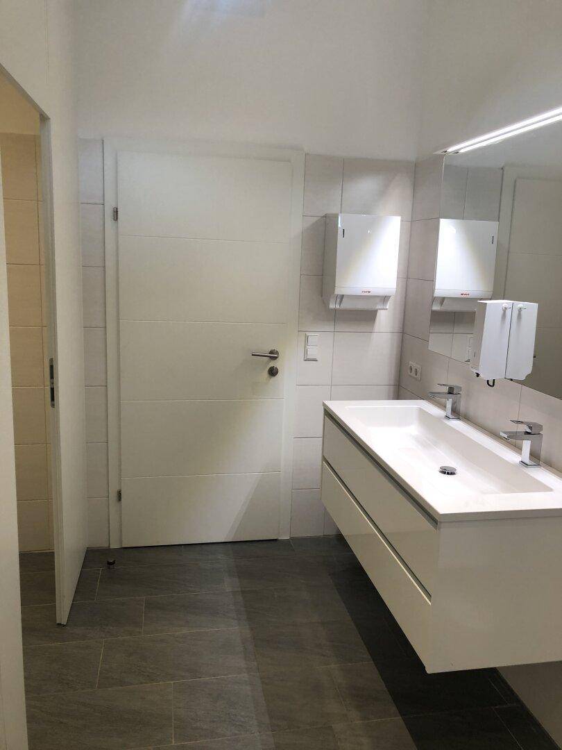 Modernes Badezimmer mit Doppelwaschbecken, großem Spiegel und grauen Fliesen auf dem Boden.
