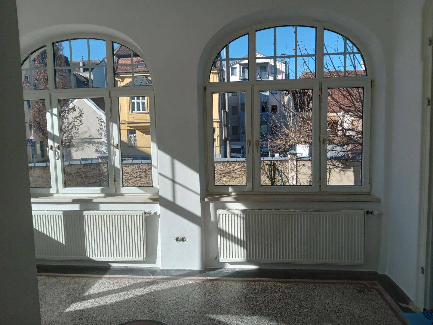 Heller Flur mit zwei großen Rundbogenfenstern, die viel Licht hereinlassen, und einem Terrazzoboden.