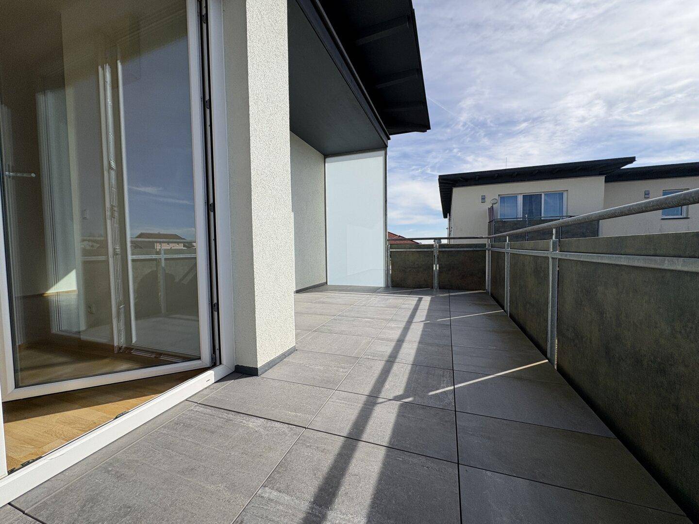 Geräumiger Balkon mit Fliesenboden und Blick auf die Umgebung, ideal zum Entspannen.