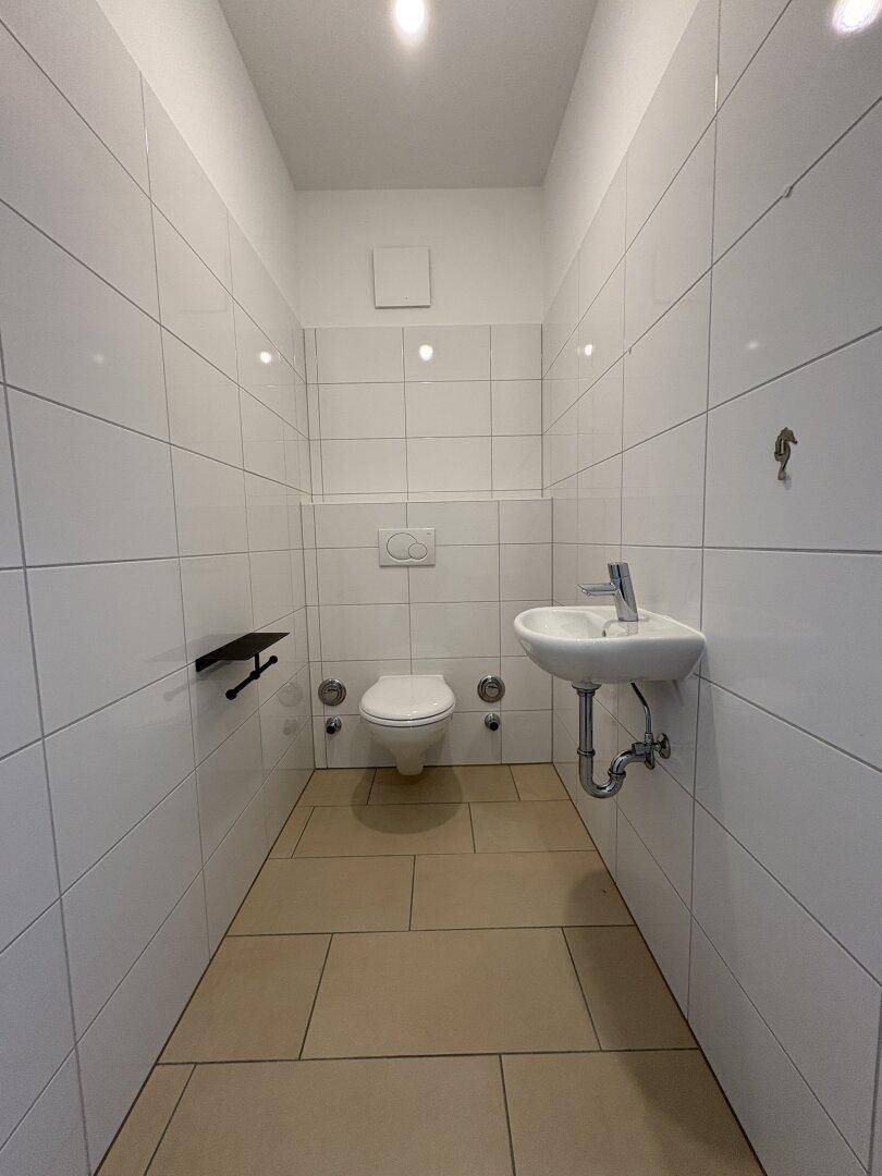 Kleines, gefliestes Gäste-WC mit Toilette und Handwaschbecken, in sauberem Zustand.