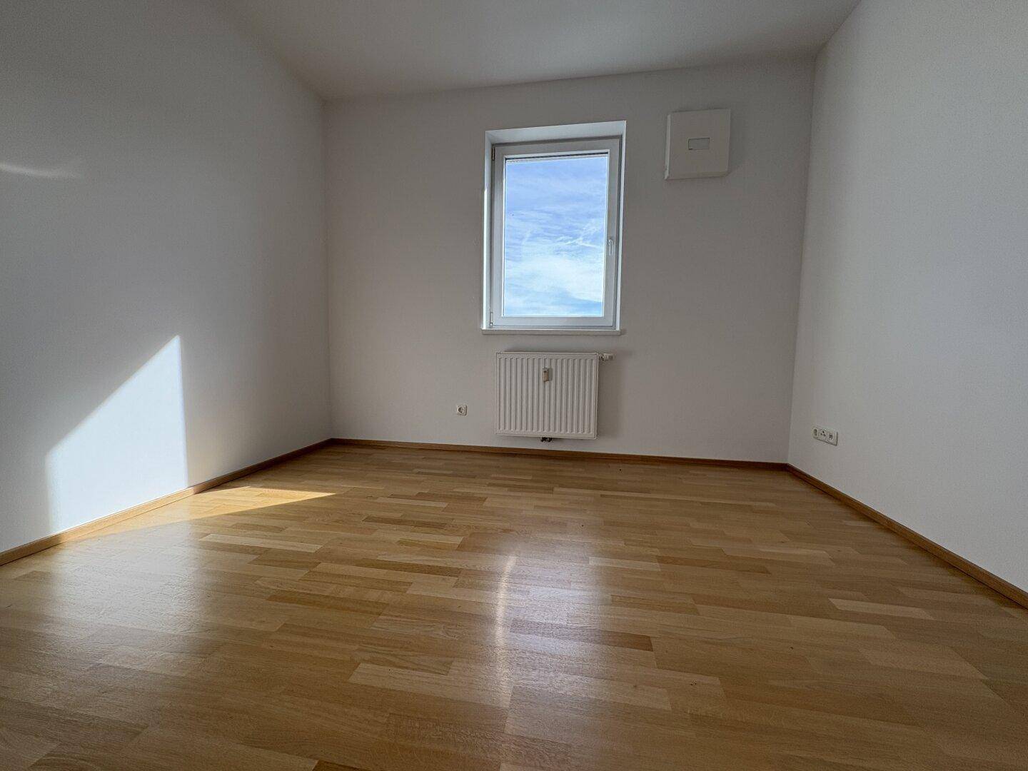 Helles Zimmer mit Parkettboden und einem Fenster, das eine angenehme Atmosphäre schafft.
