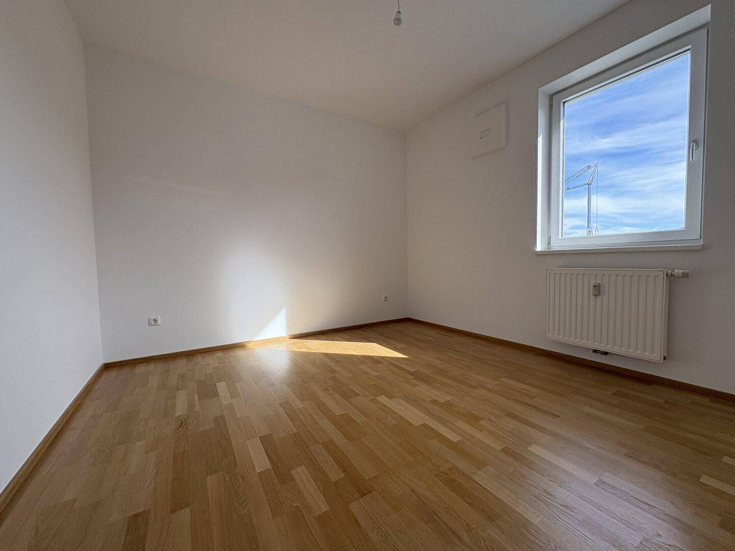 Geräumiges, helles Zimmer mit Parkettboden und einem großen Fenster für natürliche Belichtung.