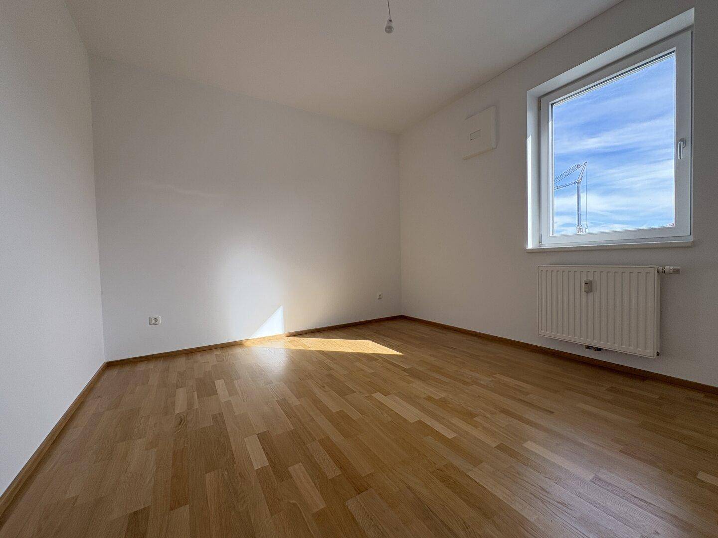Lichtdurchflutetes Zimmer mit Parkettboden und weiß gestrichenen Wänden, ideal für ein Schlafzimmer.