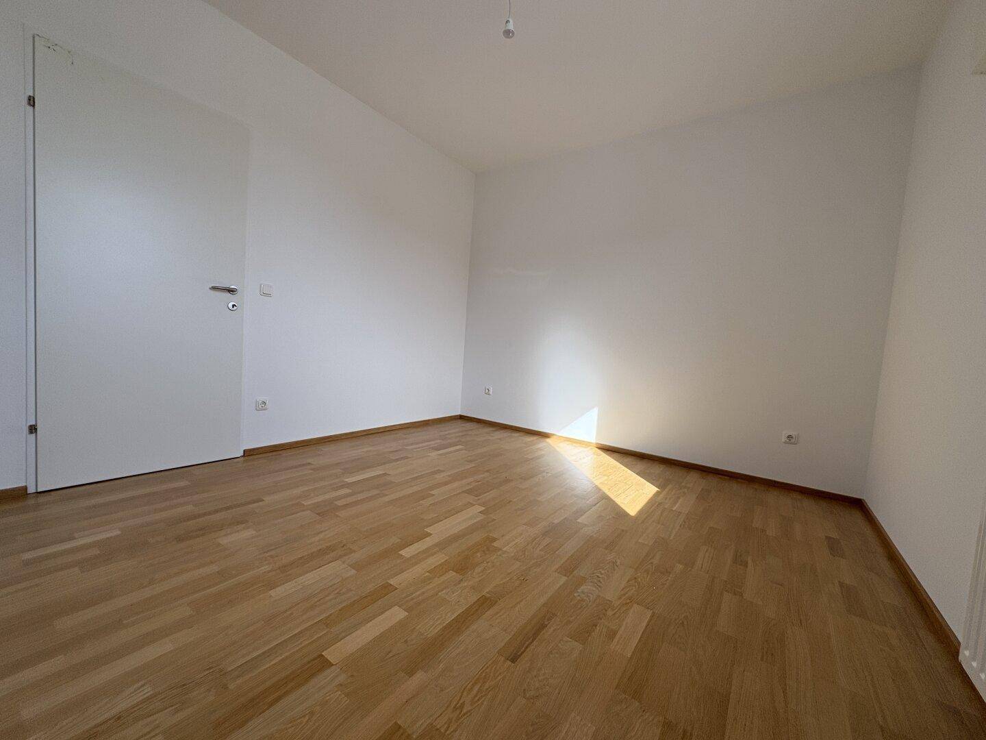 Leeres, helles Zimmer mit Parkettboden und weiß gestrichenen Wänden, bereit zur Einrichtung.