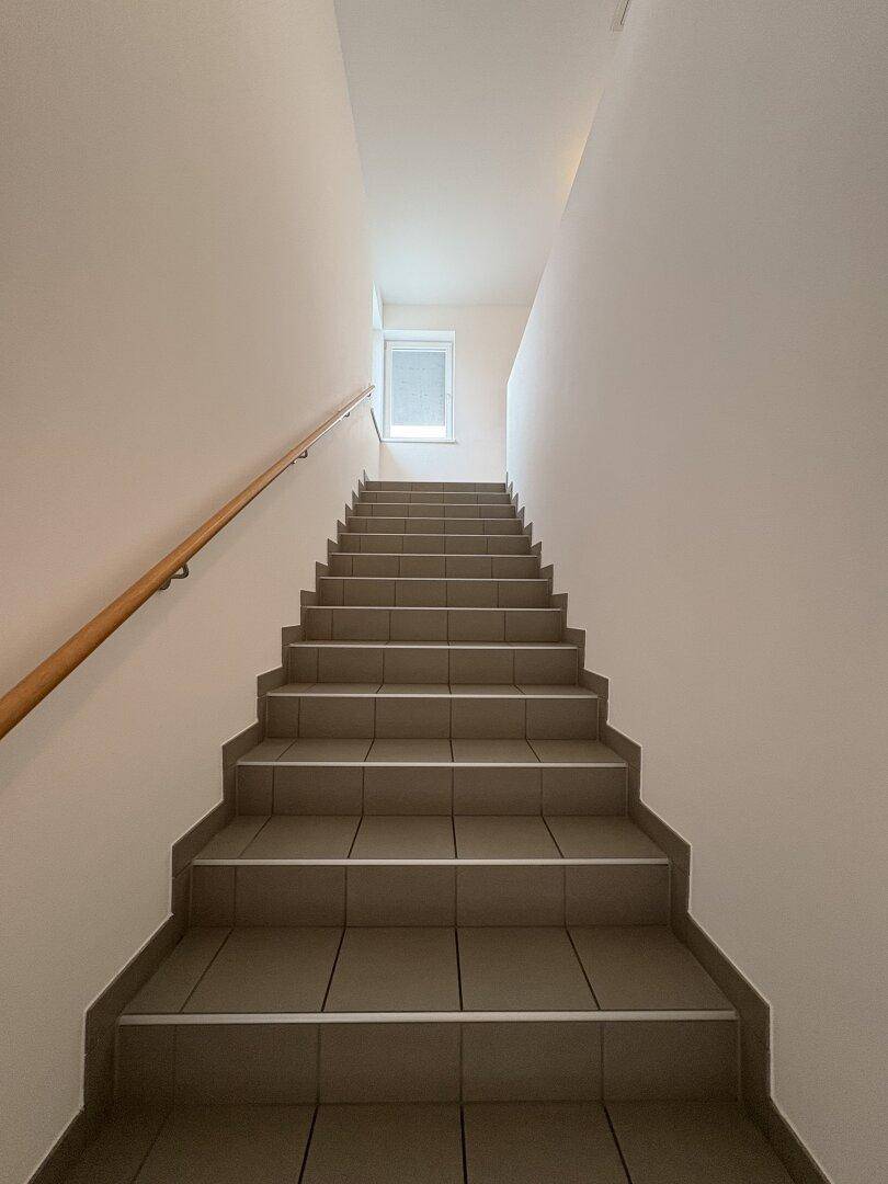 Treppenhaus mit Fliesenstufen und Holzgeländer, das zu den oberen Stockwerken führt.