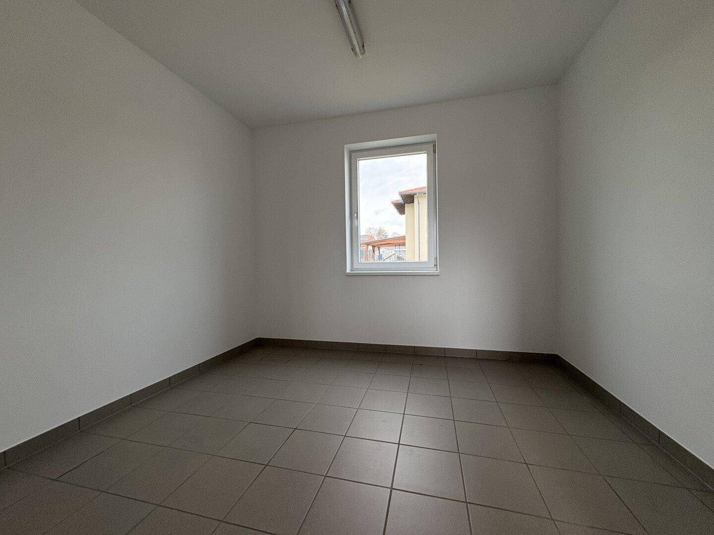Einfacher Raum mit Fliesenboden und einem Fenster, nutzbar als Abstell- oder Hauswirtschaftsraum.