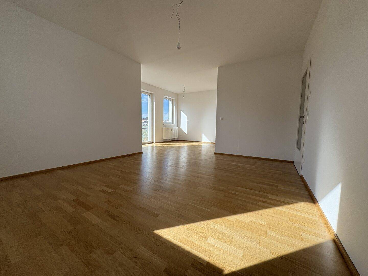 Lichtdurchfluteter Wohnraum mit Parkettboden und Zugang zu einem sonnigen Balkon.