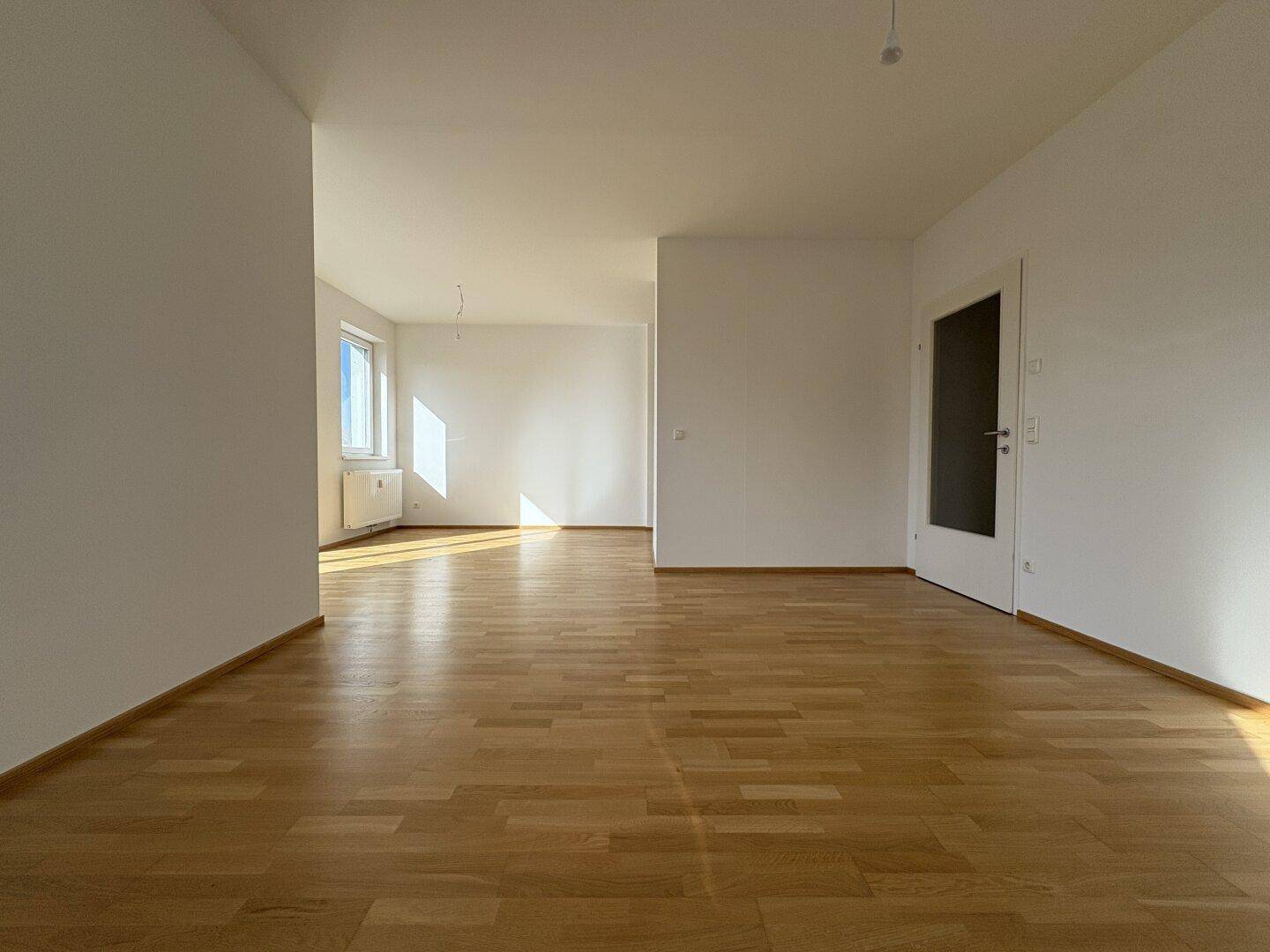 Geräumiger, heller Wohnbereich mit Parkettboden und viel Tageslicht durch die Fenster.