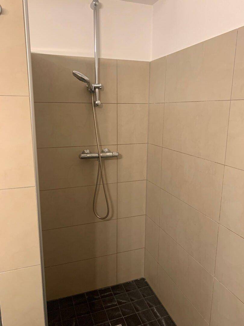 Duschbereich im Badezimmer mit beigefarbenen Fliesen und einfacher Duscharmatur.