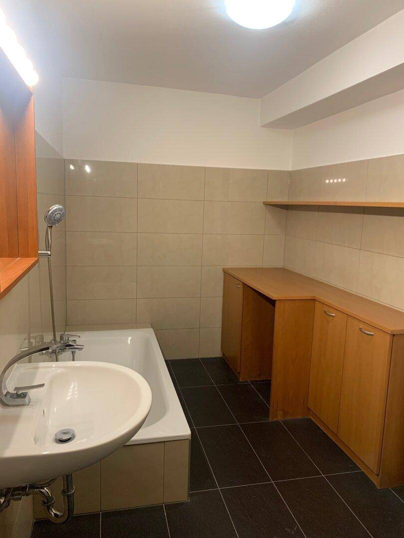 Badezimmer mit Badewanne, Waschbecken und beigefarbenen Wandfliesen sowie dunklem Boden.