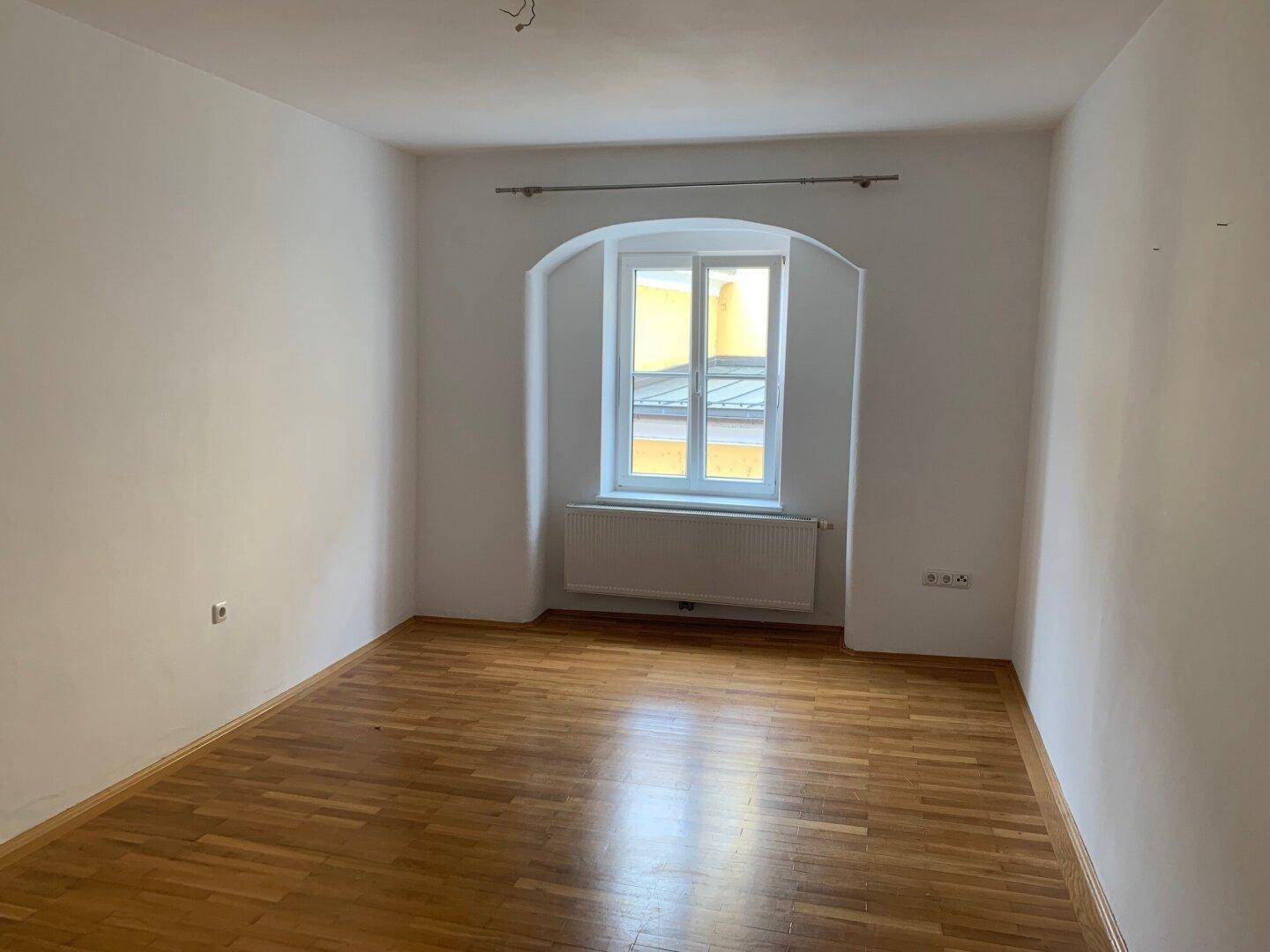 Helles Schlafzimmer mit einem charmanten Bogenfenster und warmem Parkettboden.
