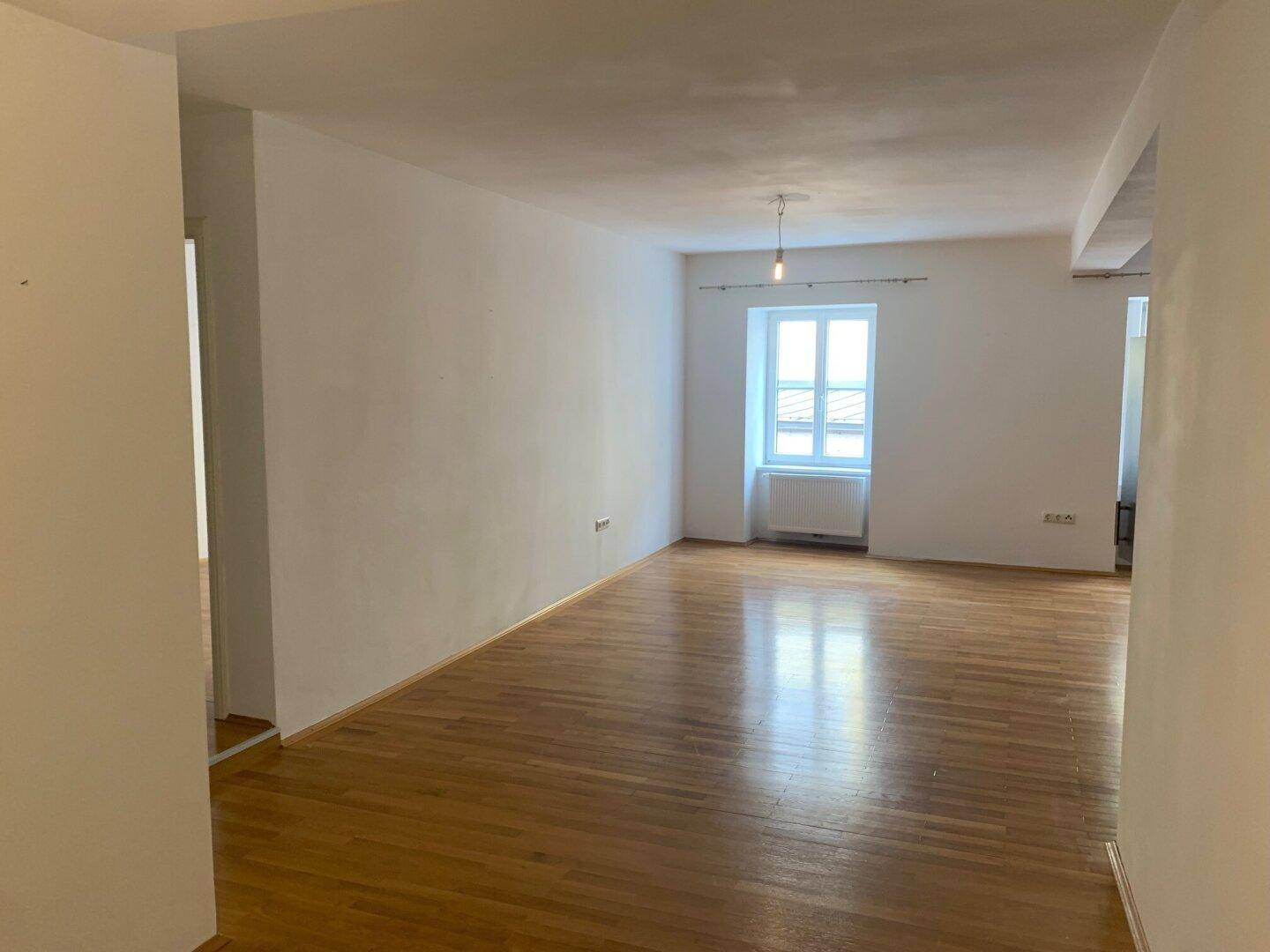 Geräumiger Wohnbereich mit einem Fenster und durchgehendem Parkettboden, der viel Licht hereinlässt.