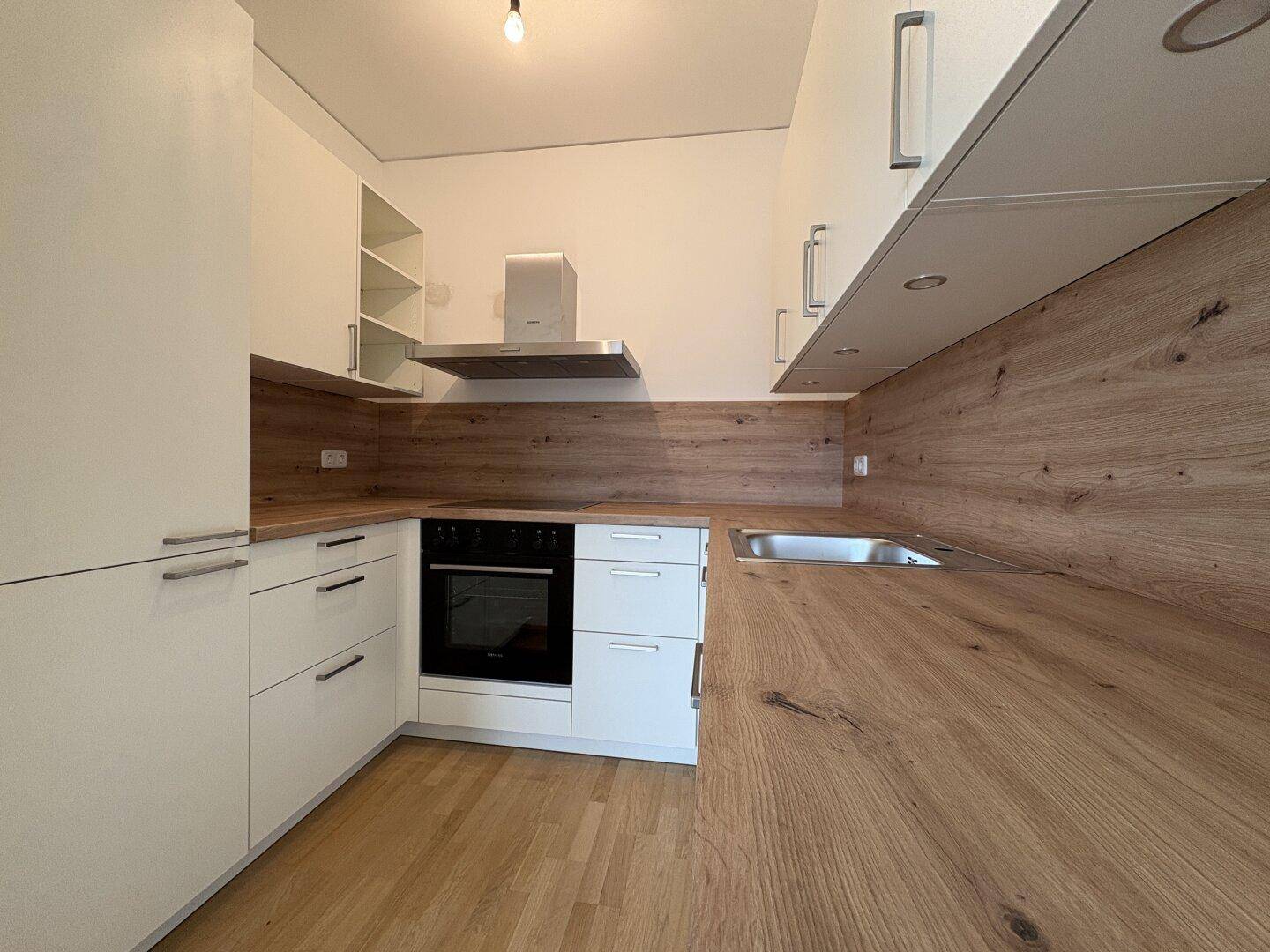 Moderne Einbauküche mit weißen Schränken, Holzoptik-Arbeitsplatten und integrierten Geräten.