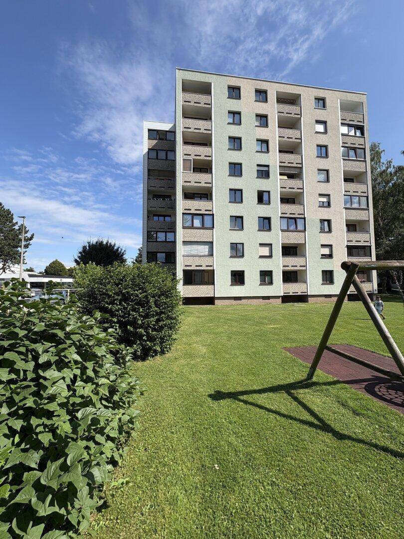 Mehrstöckiges Wohngebäude mit Balkonen und einem Spielplatz im grünen Außenbereich.