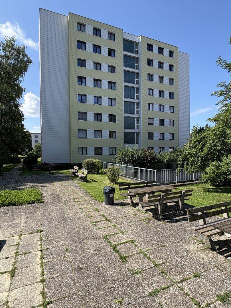 Außenbereich eines Wohnkomplexes mit Sitzgelegenheiten, Picknicktischen und Grünflächen.