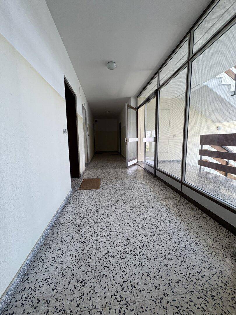 Langer Flur in einem Mehrfamilienhaus mit Terrazzoboden und natürlichem Lichteinfall.