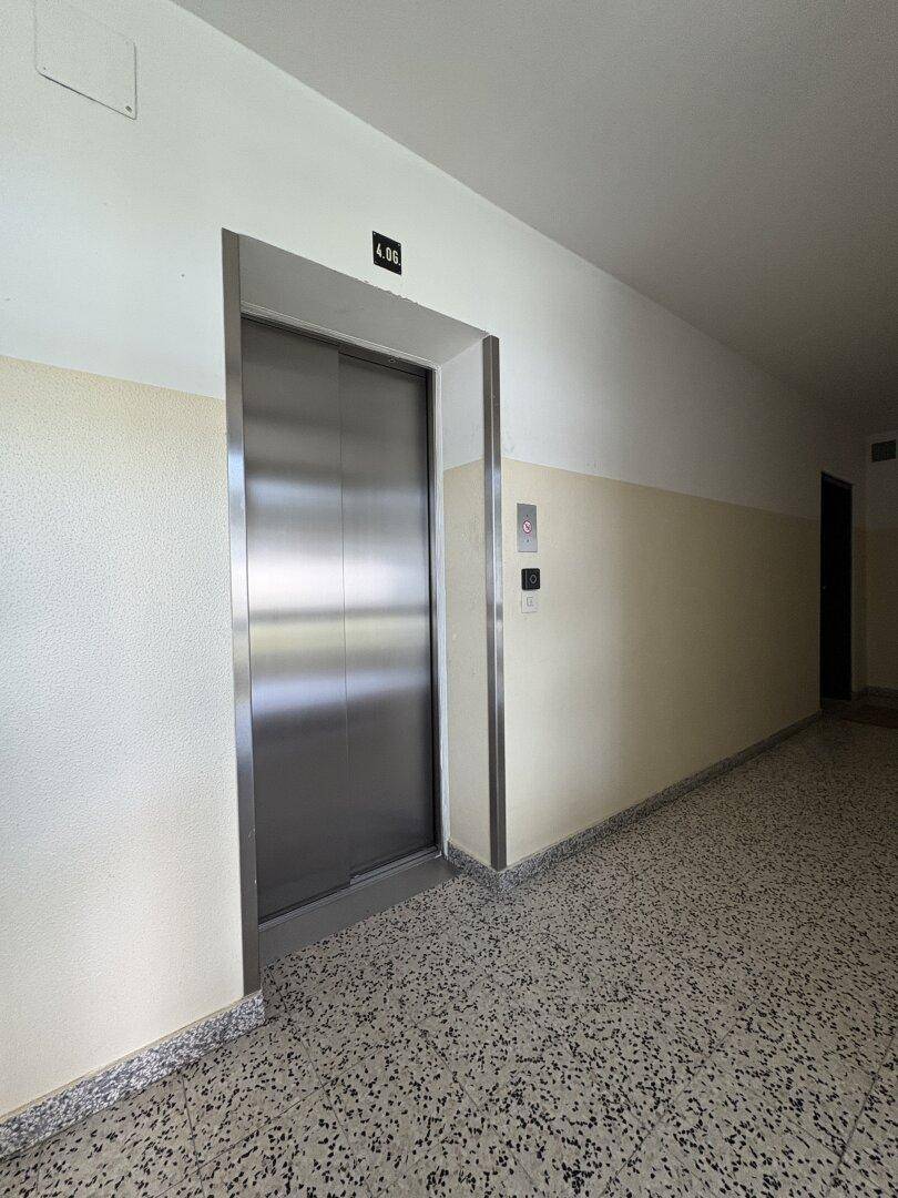 Moderner Aufzug mit Edelstahltüren in einem hellen Flur mit Terrazzoboden.
