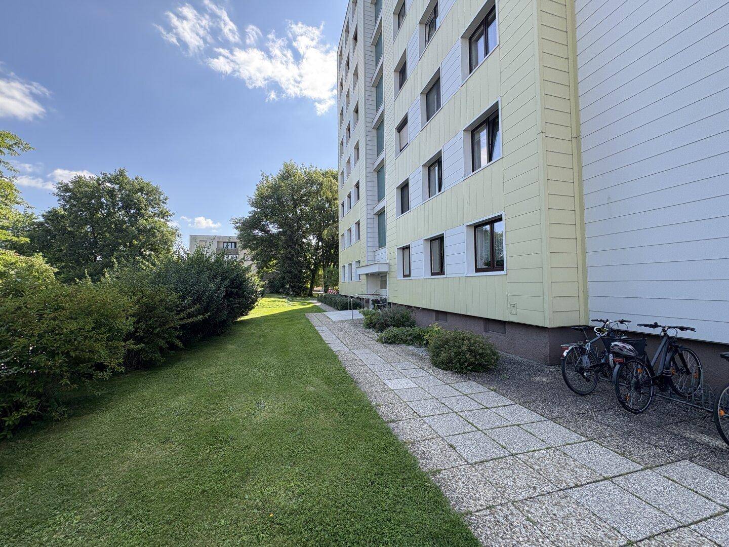 Seitenansicht des Wohngebäudes mit gepflastertem Weg, Rasenfläche und abgestellten Fahrrädern.