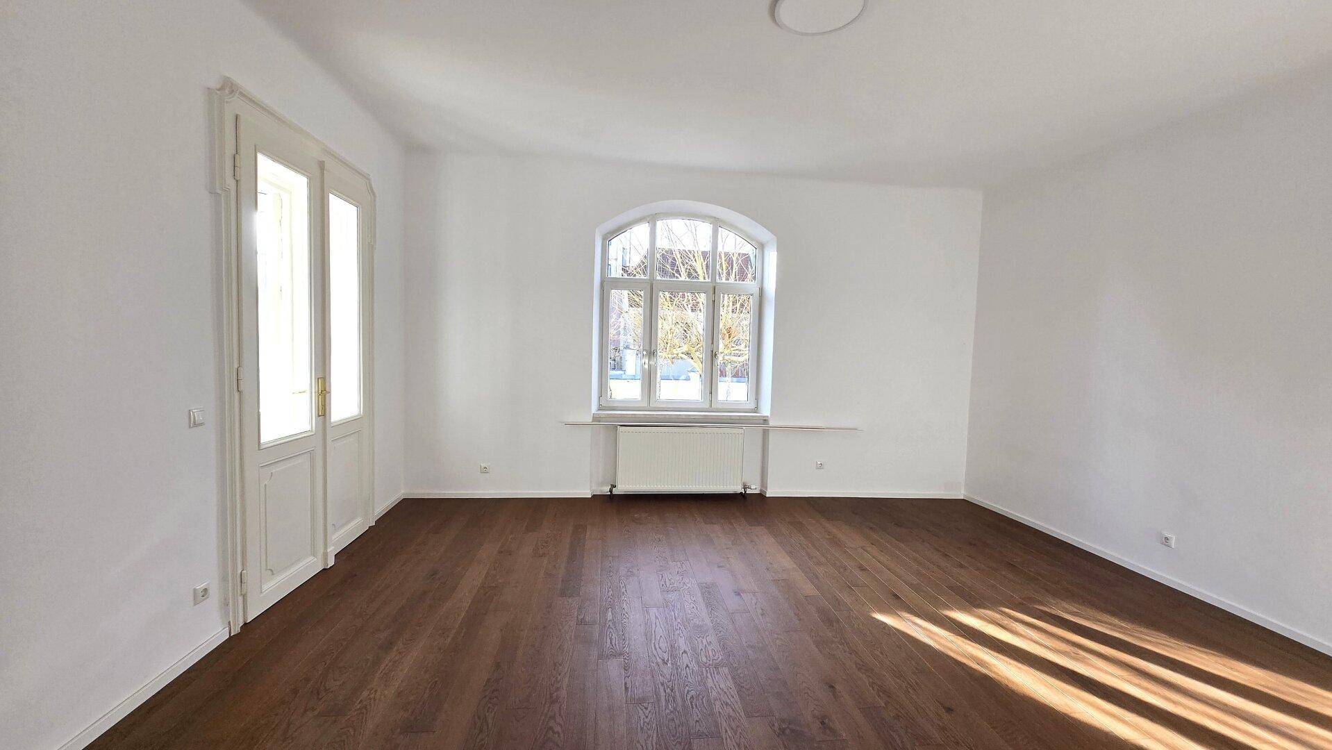 Helles, leeres Zimmer mit elegantem dunklem Holzplankenboden und einem großen, schönen Rundbogenfenster.