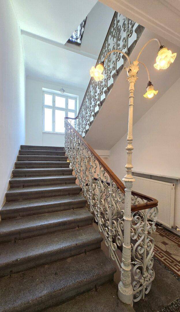 Elegantes Treppenhaus mit Steinstufen, kunstvollem Metallgeländer und einer dekorativen Laterne am Treppenabsatz.