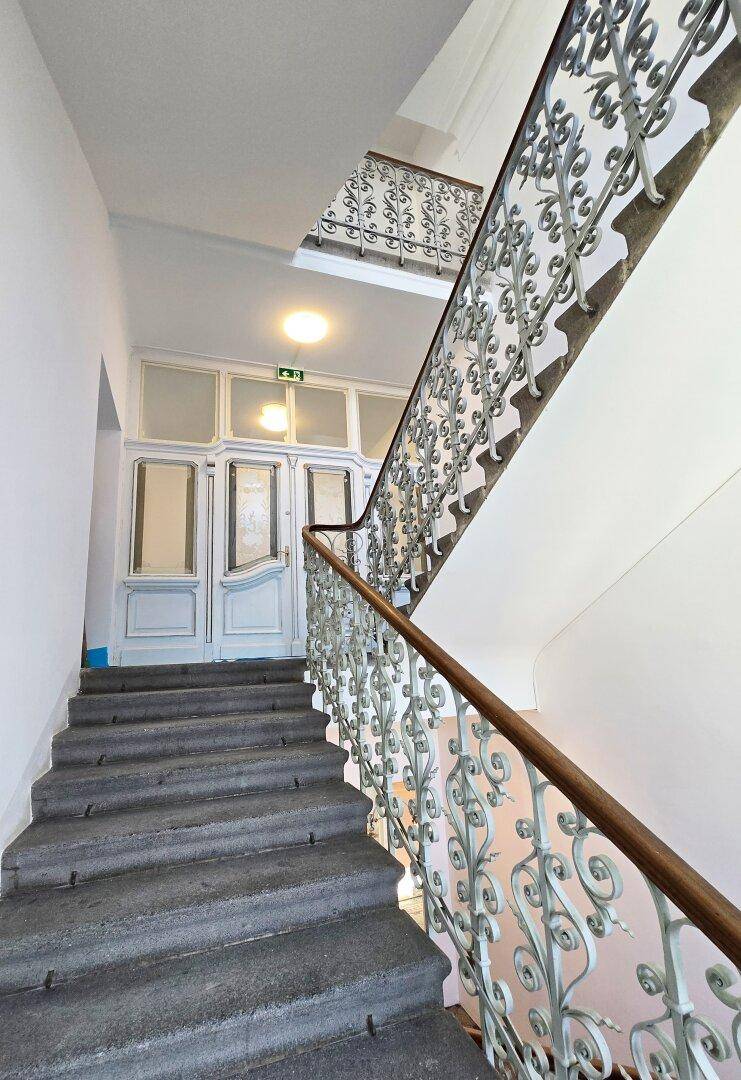 Historisches Treppenhaus mit Steinstufen und kunstvollem Geländer, das zu eleganten Doppeltüren führt.