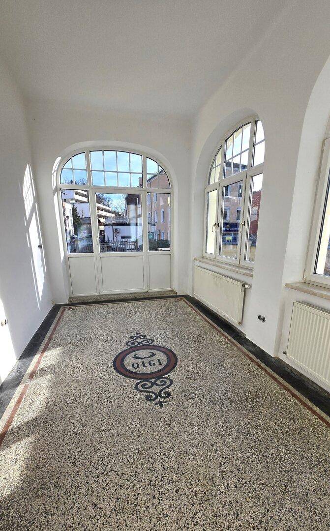 Heller Eingangsbereich mit großen Rundbogenfenstern und einer eleganten Doppeltür, die nach außen führt.