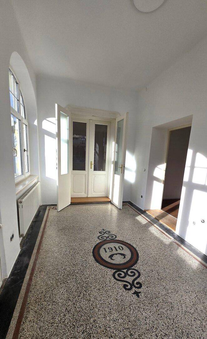 Geräumiger Eingangsbereich mit originalem Mosaikboden von 1910, hohen Fenstern und eleganten Doppeltüren.