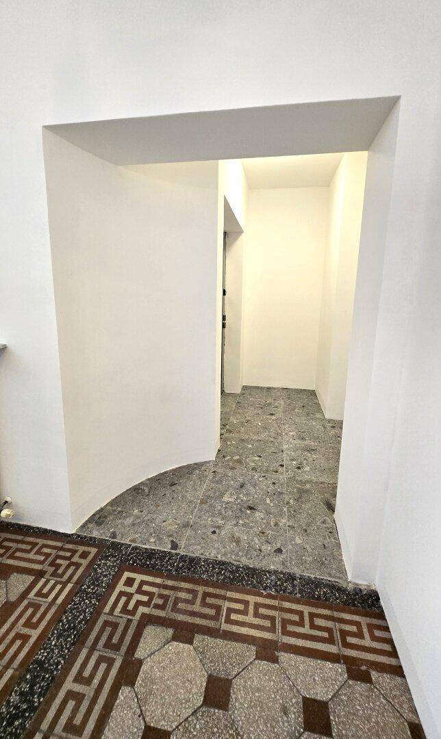 Heller Durchgang führt zu einem Flur mit modernen grauen Terrazzo-Fliesen und weiß gestrichenen Wänden.