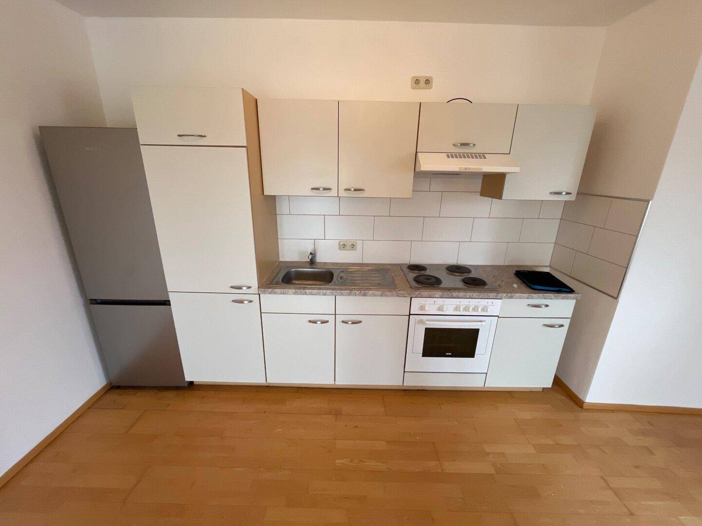 Funktionale Küchenzeile mit weißen Schränken, Herd und Kühlschrank, auf Holzboden.