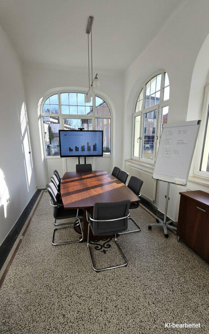 Heller Konferenzraum mit großem Besprechungstisch, Präsentationsbildschirm und gewölbten Fenstern.