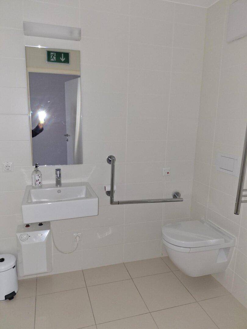 Modernes Badezimmer mit barrierefreier Ausstattung, Wand-WC, Waschbecken und Haltegriffen.