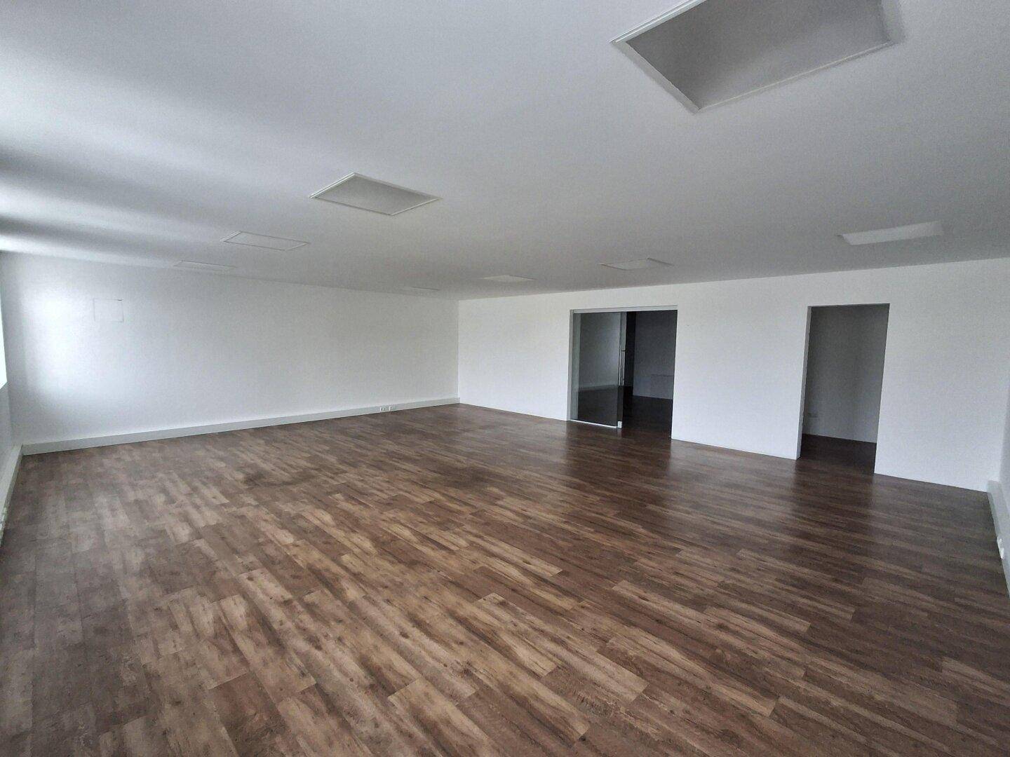 Geräumiger Gewerberaum mit Laminatboden und einer Glastür, die zu einem weiteren Bereich führt.