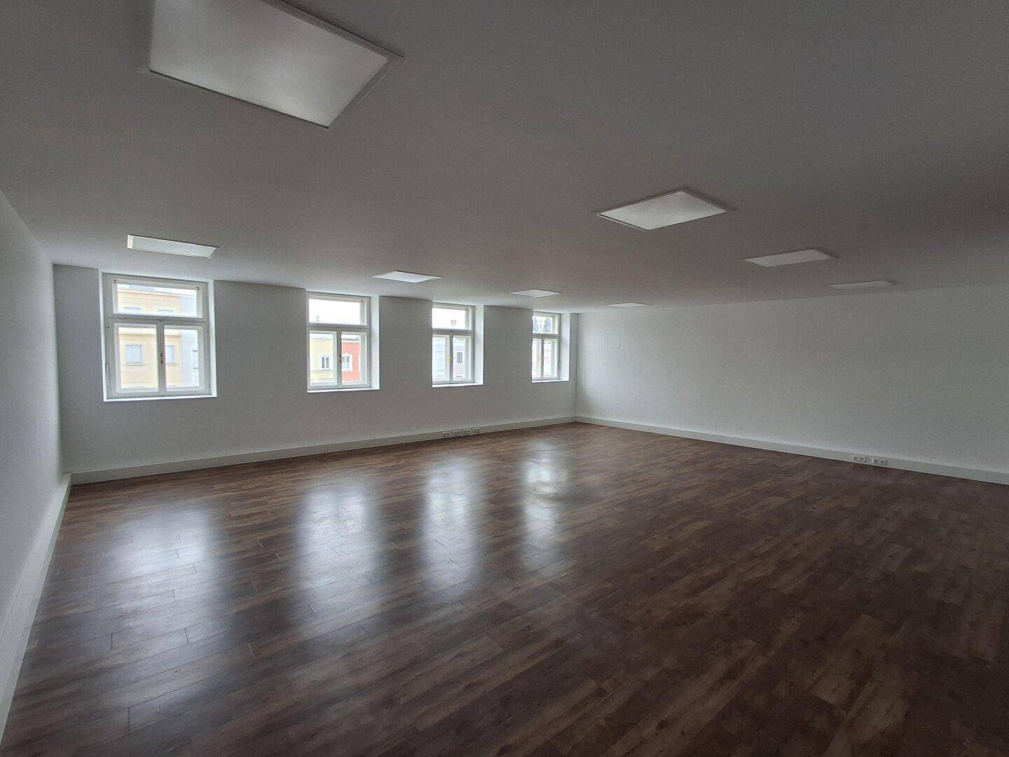 Großer, heller Gewerberaum mit vielen Fenstern und modernem Laminatboden, ideal für Büros oder Praxen.