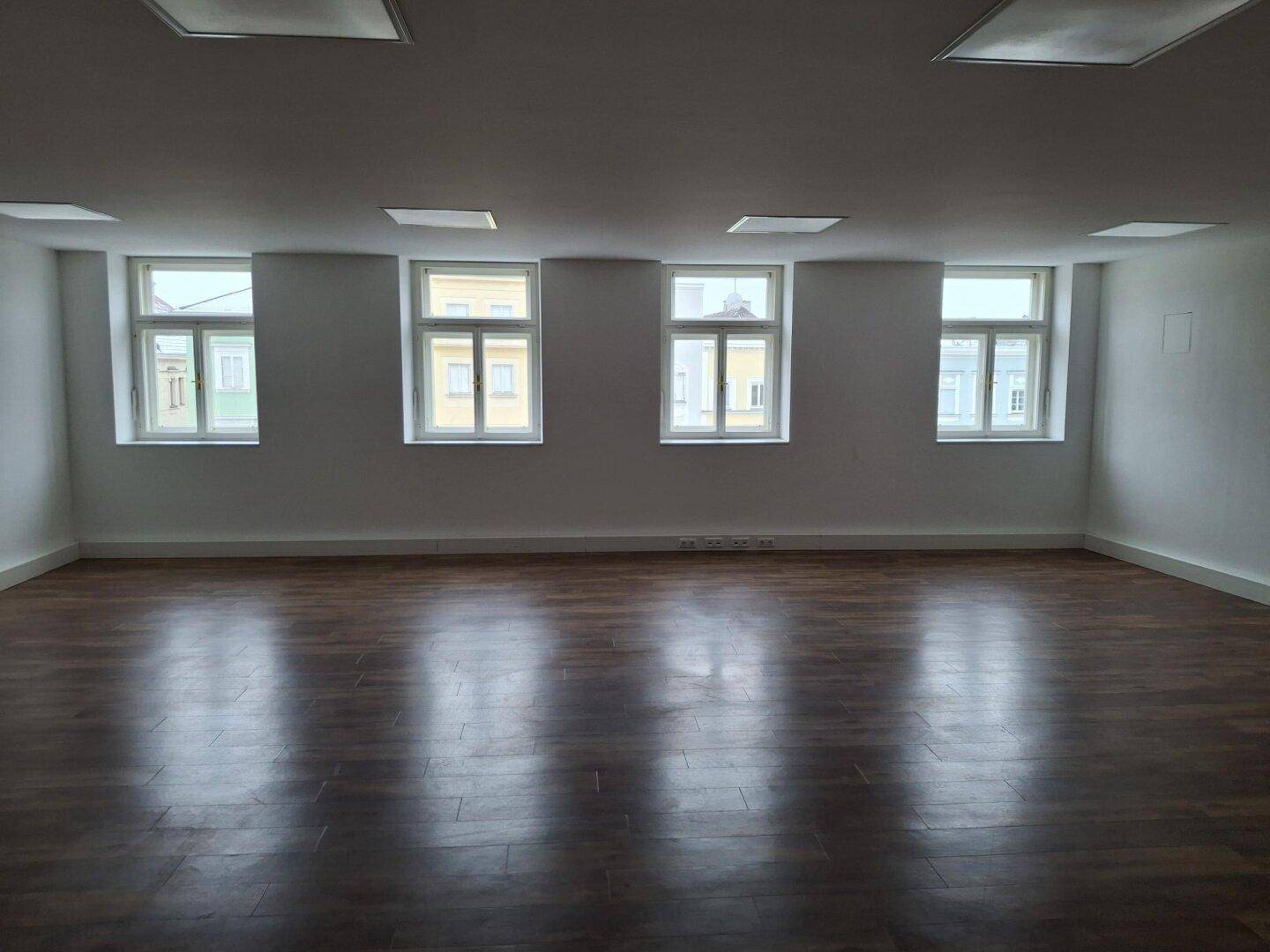 Heller Gewerberaum mit mehreren Fenstern und glänzendem Laminatboden, bereit für die individuelle Gestaltung.