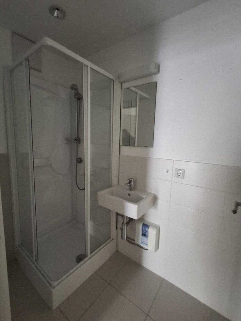 Kompaktes Badezimmer mit Duschkabine, Waschbecken und Fliesenboden, in gutem Zustand.