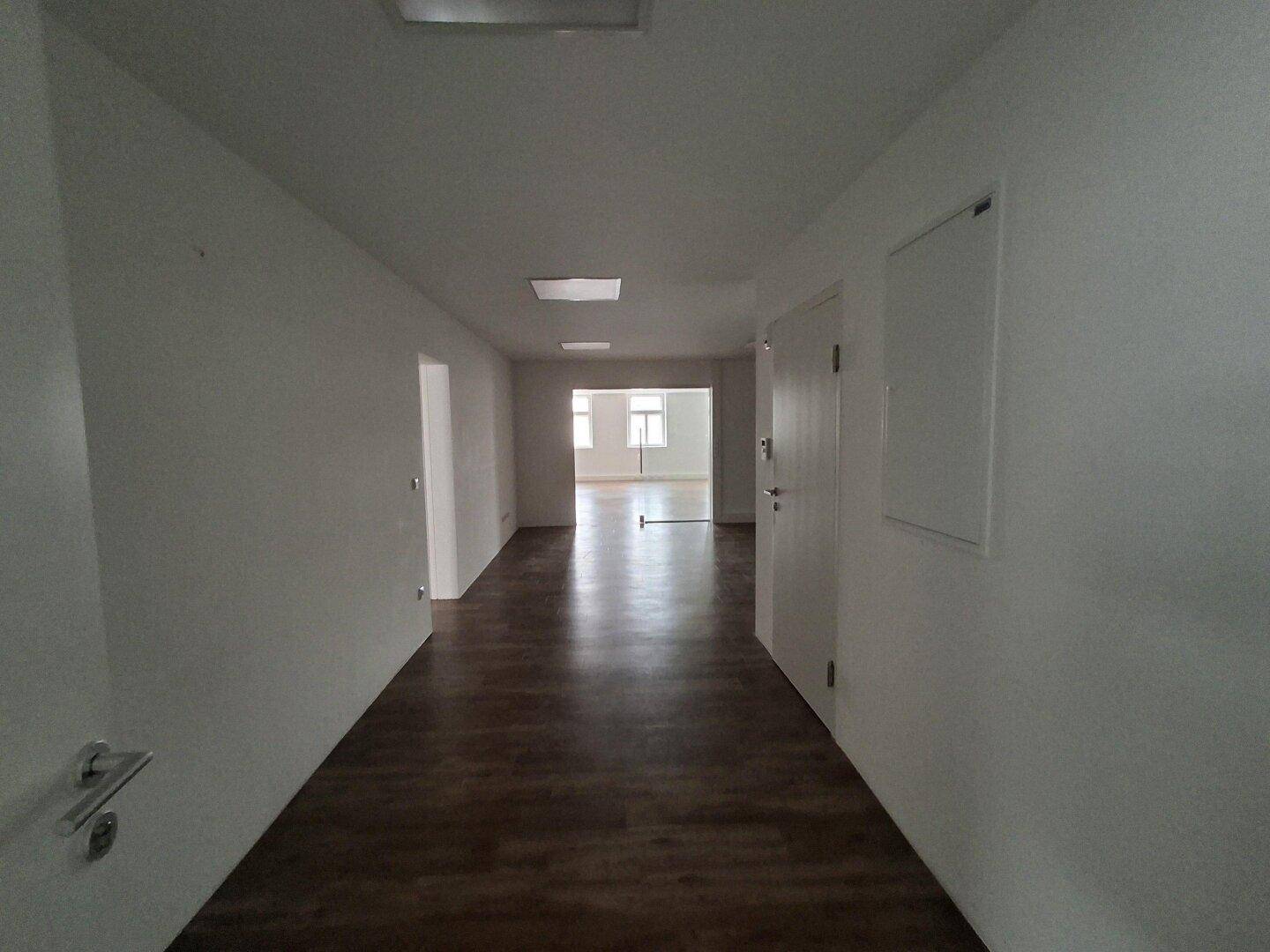 Langer, heller Flur mit Laminatboden und mehreren Türen, der zu verschiedenen Räumen führt.