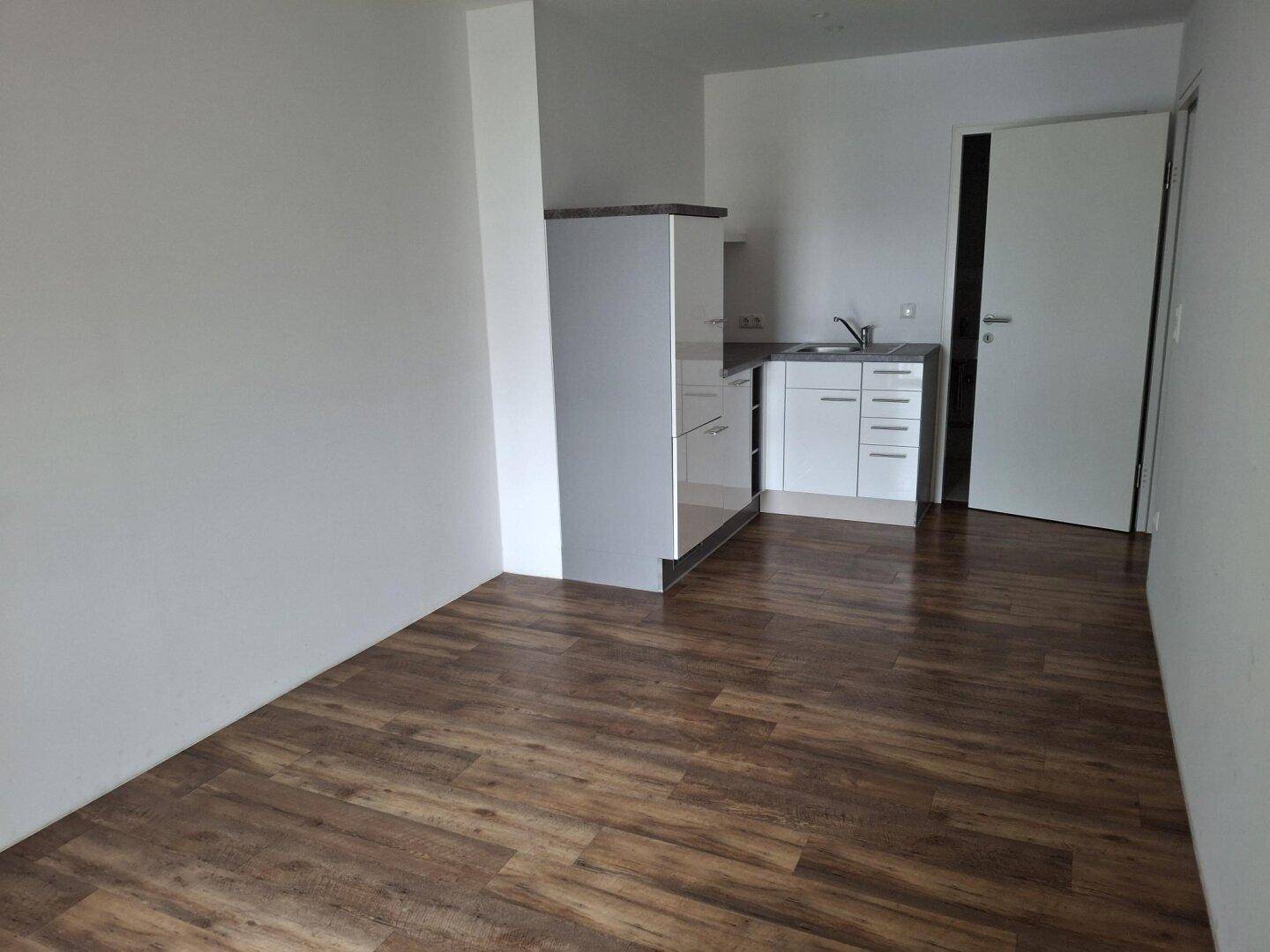 Heller Raum mit integrierter Küchenzeile und Laminatboden, ideal für ein kleines Büro oder Studio-Apartment.