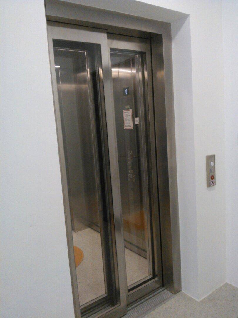 Moderner Aufzug mit Edelstahltüren und einem Bedienfeld in einem hellen Flur, bietet bequemen Zugang zu allen Etagen.