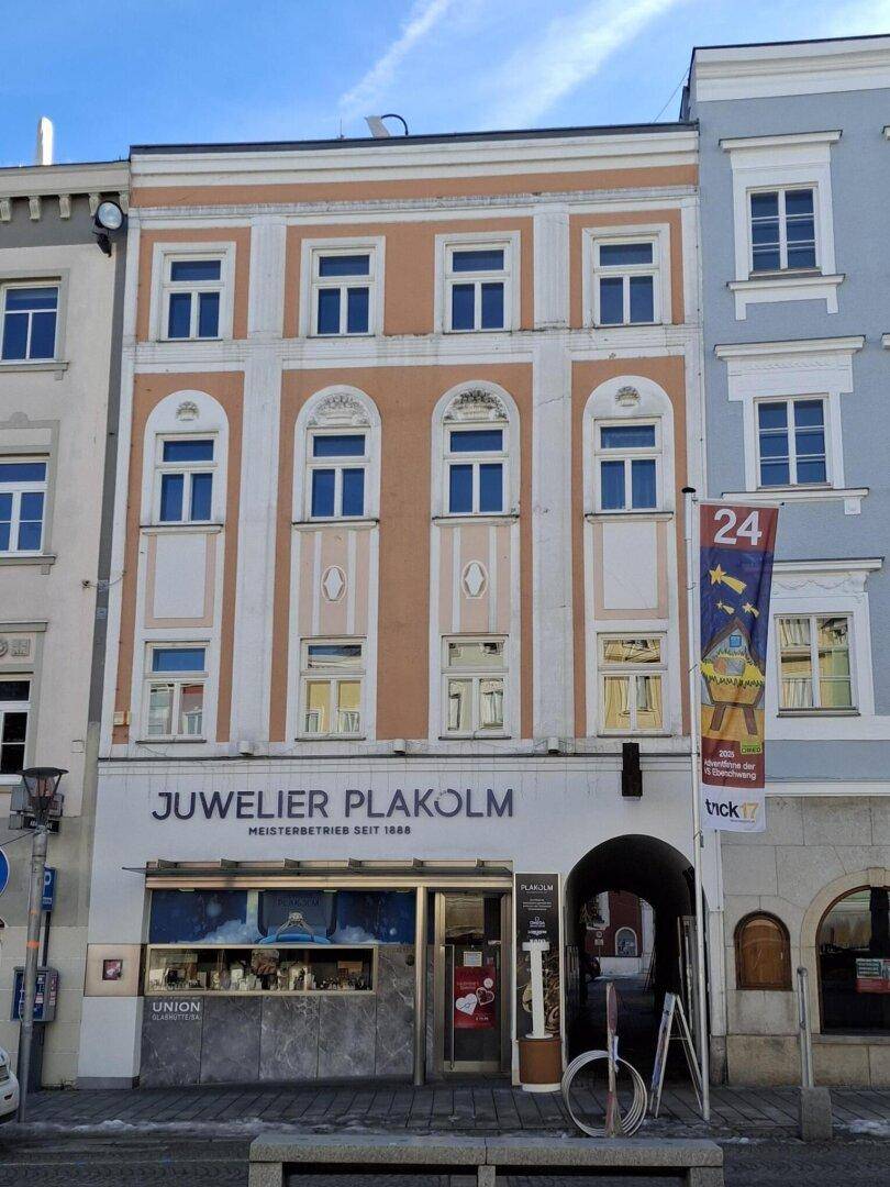 Historische Fassade eines Gebäudes mit Ladenlokal im Erdgeschoss und Wohnungen darüber, unter blauem Himmel.