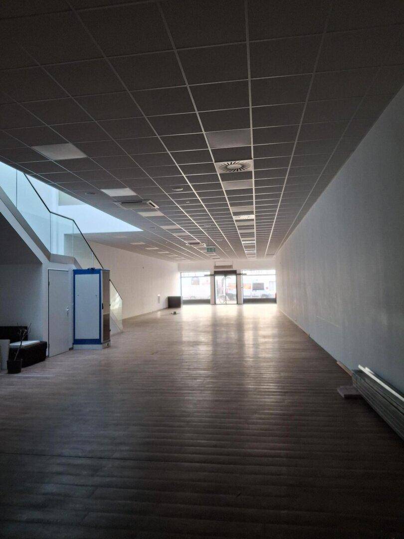 Leerer Einzelhandelsraum mit Holzboden, hohen Decken und großen Fenstern am Eingangsbereich, bereit zur Gestaltung.